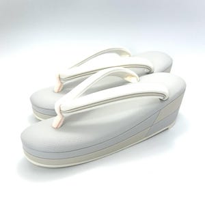 May include: A pair of light gray platform sandals with a textured finish and white thong straps. The sandals feature a multi-layered sole design with a subtle beige accent layer and pale pink details at the base of the straps, providing a clean look.