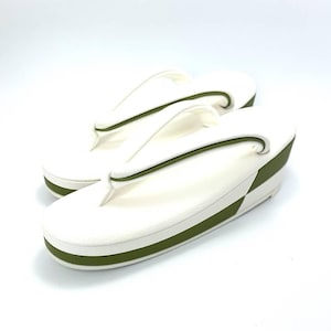 May include: A pair of white zori sandals featuring a thick platform sole with a horizontal olive green stripe. The thong-style straps are white with a thin olive green accent line running along the center, designed for a slip-on fit with a raised heel.