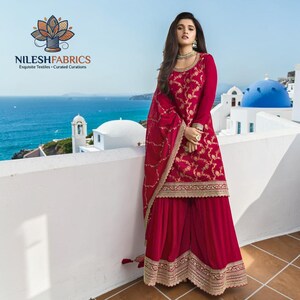 May include: A vibrant red ensemble featuring a long-sleeved top with gold embroidery and wide-leg pants. The outfit includes a matching scarf. The image also displays the "NILESH FABRICS" logo with the tagline "Exquisite Textiles - Curated Curations".