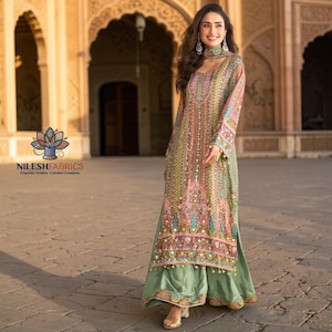 Peut inclure: Une femme porte une longue robe à motifs dans des tons de vert, rose et or. La robe présente des détails complexes et des manches longues. Le texte "NILESHFABRICS" est visible. La robe semble être un vêtement traditionnel.