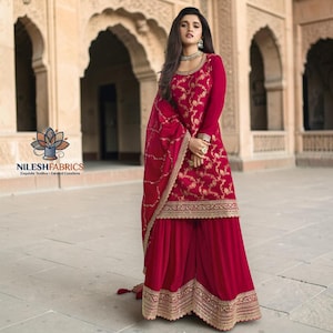 Puede incluir: Un salwar kameez rojo bordado con un dupatta a juego. El atuendo presenta bordados florales dorados en el corpiño y los bordes. El conjunto lo lleva una persona en un entorno al aire libre.