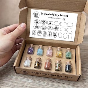 Op de afbeelding: Een kartonnen doos met twaalf kleine glazen flesjes met kurken, gevuld met kleurrijke kristallen en glitter. De doos bevat ook een vel met bedrukbare etiketten met de tekst "Enchanted Fairy Potions".