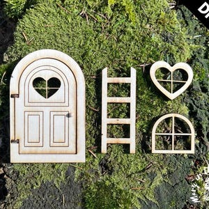 Könnte beinhalten: Ein DIY-Kit für einen Feengarten, mit einer Holztür mit herzförmigem Fenster, einer Leiter, einem herzförmigen Fenster und einem Bogenfenster. Die Teile sind aus hellem Holz gefertigt und vor einem moosigen Hintergrund platziert. Die Worte "DIY KIT" sind in Schwarz gedruckt.