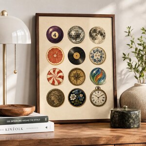 May include: A framed wall art print featuring a grid of twelve circular illustrations including a number four billiard ball, a disco ball, the moon, a grapefruit slice, a vinyl record, a blue floral plate, a peppermint candy, a compass, a marble, a coin, a flower medallion, and a pocket watch.