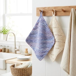 Peut inclure: Deux maniques tricotées, une en fil multicolore bleu et violet et l'autre en crème, sont suspendues à un porte-serviettes en bois. Une serviette en lin beige est suspendue à droite. Les maniques sont en forme de losange avec une boucle pour suspendre.