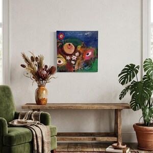 Puede incluir: Una pintura sobre lienzo cuadrada que presenta un fondo de cielo nocturno azul oscuro con un grupo central de flores blancas, dos ojos estilizados prominentes y formas abstractas en tonos rojos, naranjas, verdes y amarillos, creando una composición.