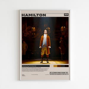 Puede incluir: Un póster rectangular con el título HAMILTON y el año 2020 en la parte superior. El centro muestra una escena con un intérprete con un abrigo marrón, chaleco azul y calzones amarillos del siglo XVIII. El texto inferior incluye créditos.