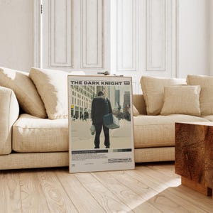 May include: A rectangular movie poster for The Dark Knight 2008 featuring a central illustration of a person in a dark suit carrying a blue bag and a clown mask. The poster includes the film title, director credit, and a PG-13 rating symbol.
