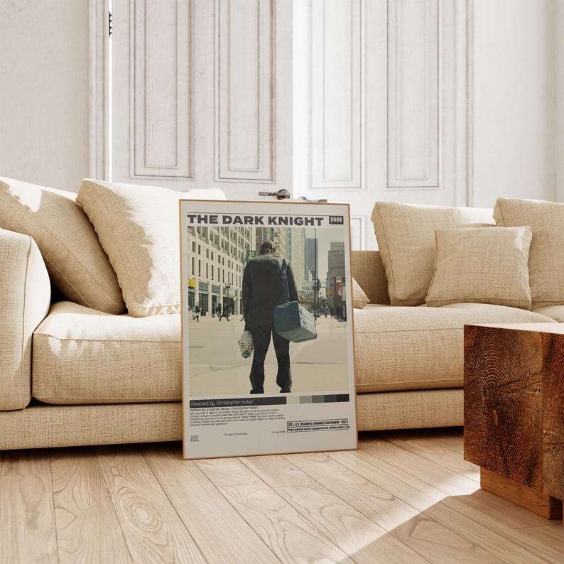 May include: A rectangular movie poster for The Dark Knight 2008 featuring a central illustration of a person in a dark suit carrying a blue bag and a clown mask. The poster includes the film title, director credit, and a PG-13 rating symbol.