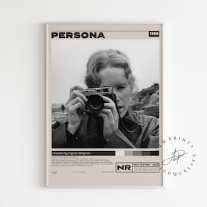 May include: A framed black and white movie poster for the film "Persona" from 1966. The poster features a woman holding a camera, with the film title at the top and credits at the bottom. The poster has a neutral color palette.