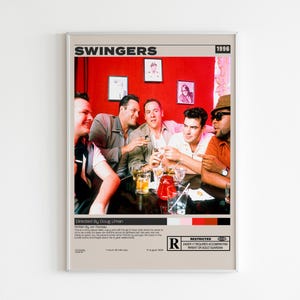 Puede incluir: Un póster de la película Swingers de 1996 que muestra a un grupo de personas sentadas a una mesa frente a una pared de color rojo brillante. El cartel incluye el título Swingers en la parte superior, una escena de la película y un recuadro negro.
