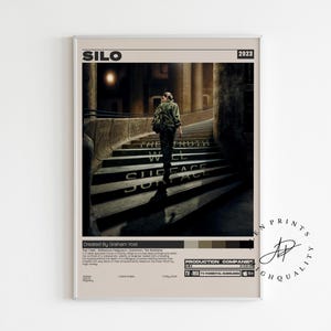 May include: A framed poster titled "SILO" from 2023. The image shows a person ascending a staircase with the words "THE TRUTH WILL SURFACE" printed on the steps. The poster has a neutral colour palette and a minimalist design.