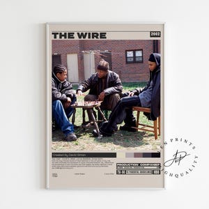 May include: A framed poster featuring the title "THE WIRE" and the year "2002". The image shows three people seated, playing chess. The poster has a neutral color palette with text at the bottom.
