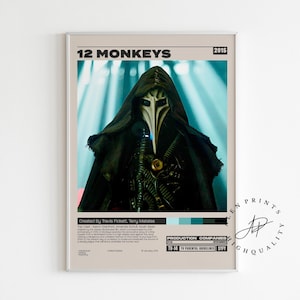 May include: A framed poster for the film "12 Monkeys" featuring a figure in a black hooded cloak and a white mask. The poster has the film title and the year 2015 at the top. The poster has a light beige background.