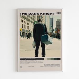 May include: A framed movie poster for The Dark Knight, 2008. The poster features a person in a black suit seen from behind, carrying a blue duffel bag and holding a clown mask. The text includes the title, director, and a brief plot summary.