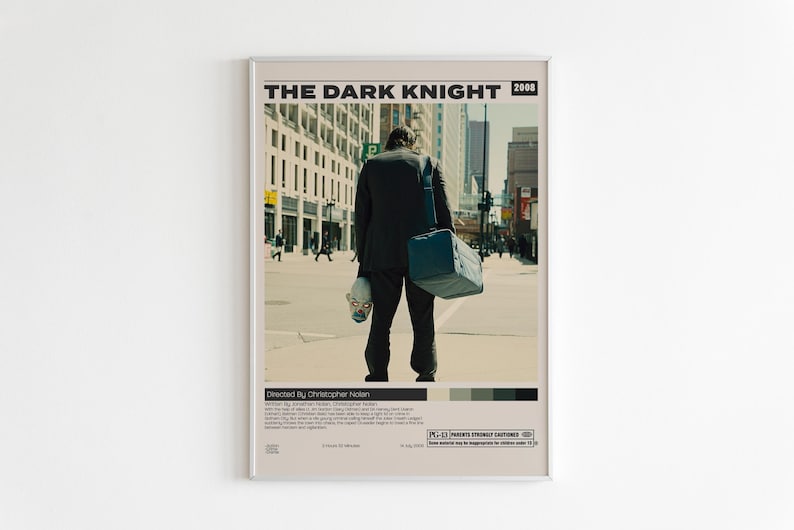 May include: A framed movie poster for The Dark Knight, 2008. The poster features a person in a black suit seen from behind, carrying a blue duffel bag and holding a clown mask. The text includes the title, director, and a brief plot summary.