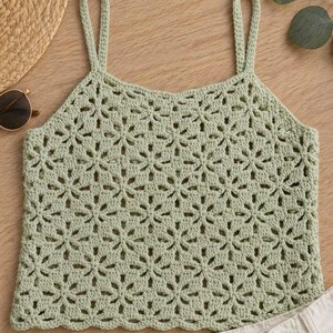 May include: A light green crochet top with a floral pattern. The top has thin straps and a scalloped hem. The top is made of a soft, breathable material, perfect for warm weather.