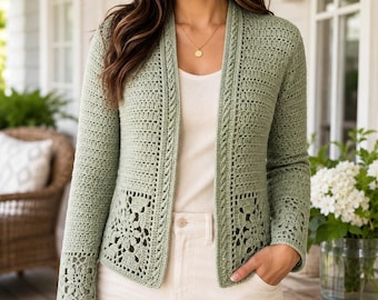 May include: A sage green open-front cardigan featuring intricate crochet work with floral motifs at the lower panels and cuffs, long sleeves, and a textured stitch pattern throughout the body, worn over a plain white top and light-coloured trousers.