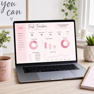 May include: A laptop shows a pink and white task tracker dashboard. A pink mug with "good day" text, a succulent, and a notebook with "plan do review" text are on the desk. A framed print with "you can" text is in the background.