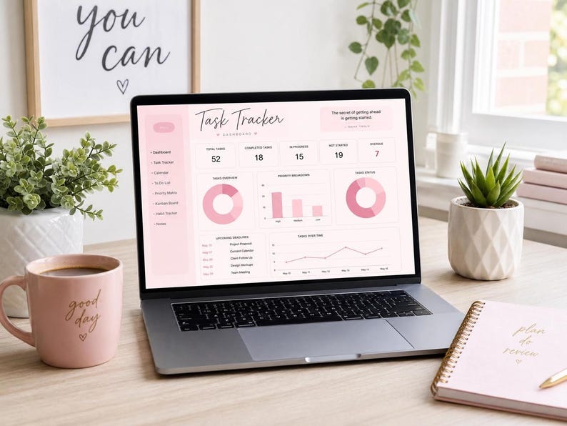 May include: A laptop shows a pink and white task tracker dashboard. A pink mug with "good day" text, a succulent, and a notebook with "plan do review" text are on the desk. A framed print with "you can" text is in the background.