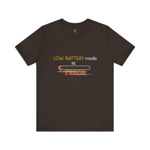 May include: Dark brown t-shirt with the text "LOW BATTERY mode 1% ERROR" in yellow, red, and green. The design features a battery icon and a glitch effect, creating a tech-inspired aesthetic.