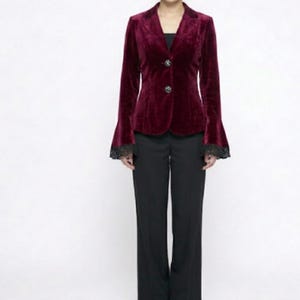 May include: A burgundy velvet blazer with bell sleeves and black lace trim. The blazer has two decorative buttons and is paired with black trousers. The outfit is a formal style.