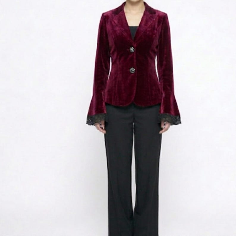 May include: A burgundy velvet blazer with bell sleeves and black lace trim. The blazer has two decorative buttons and is paired with black trousers. The outfit is a formal style.