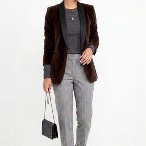 May include: A brown velvet blazer with a black lapel, paired with a gray ribbed sweater and gray pinstripe pants. A black purse with a chain strap completes the outfit. The ensemble is suitable for business or casual wear.