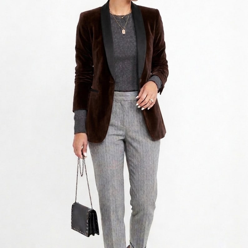 May include: A brown velvet blazer with a black lapel, paired with a gray ribbed sweater and gray pinstripe pants. A black purse with a chain strap completes the outfit. The ensemble is suitable for business or casual wear.