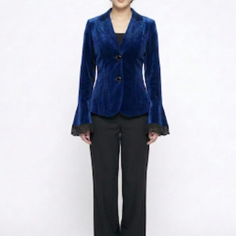 May include: A vibrant blue velvet blazer with a notched lapel and a two-button fastening. The long sleeves feature flared cuffs with black lace trim. The blazer is worn with black trousers, forming a smart outfit.