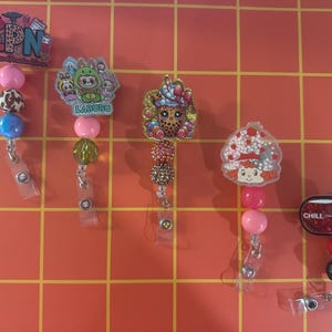 Puede incluir: Cinco coloridos portatarjetas retráctiles con varios diseños. Uno tiene el texto "LPN", otro presenta un personaje de dibujos animados y un tercero tiene un estampado de leopardo. El cuarto tiene un diseño de fresa y el último tiene el texto "CHILL".