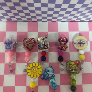 Puede incluir: Una colección de carretes de insignia coloridos con varios diseños de personajes, incluyendo Stitch, Minnie Mouse y un girasol sonriente. Cada carrete presenta cuentas decorativas en colores coordinados y un cordón retráctil.