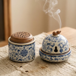 以下が含まれることがあります： 青い花柄のセラミック香炉が2つ。1つは茶色の蓋が付いた円筒形で、もう1つは小さな開口部とひょうたん型のトップが付いた球形です。球形のバーナーから煙が立ち上っています。
