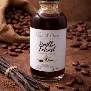 Könnte beinhalten: Eine klare Glasflasche Vanilleextrakt mit schwarzem Verschluss, beschriftet mit "Second Oven Bakery Vanilla Extract". Das Etikett listet Zutaten und Größe, 50 ml. Vanilleschoten und Kakaobohnen sind um die Flasche herum verstreut.