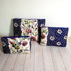 May include: Three zippered pouches in varying sizes, each featuring a dark blue fabric with a small white floral pattern and a central vertical panel displaying a larger, colorful floral print in shades of pink, green, and blue with a cream background.