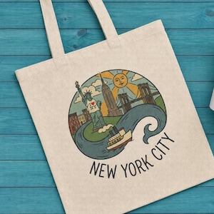 May include: A canvas tote bag and a ceramic mug with a New York City design. The design features the Statue of Liberty, the Empire State Building, a bridge, and a boat, with the words "New York City". The mug has a red interior and handle.