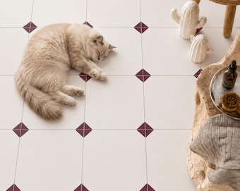 May include: A light beige cat sleeping on a white floor tile pattern featuring small dark red diamond accents at the corners. Nearby are two white ceramic cactus figurines, a wooden stool with folded towels, and a rustic wooden side table.