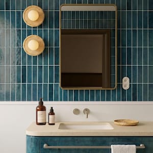 Op de afbeelding: Een moderne badkamer met een turquoise betegelde muur, een goudomrande spiegel en een turquoise wastafel. Twee ronde wandkandelaars met warme gloeilampen zijn aan de muur bevestigd. De wastafel heeft een wastafel, kraan en een klein geweven dienblad.