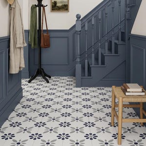 May include: A hallway floor featuring white square tiles with a repeating pattern of dark blue and light gray flower motifs. The space includes a wooden stool with a woven seat, a black coat rack, and blue wainscoting along the walls.
