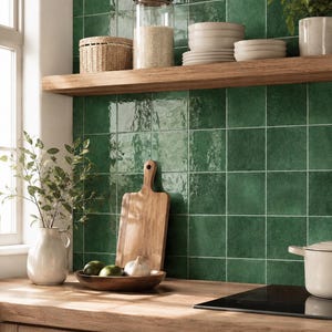 May include: A kitchen wall featuring square, glossy, deep green ceramic tiles with a subtle textured finish. The tiles are arranged in a grid pattern, creating a vibrant backdrop for the wooden countertop, floating shelf, and various kitchen items.