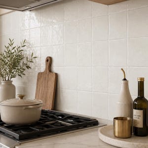 Puede incluir: Una escena de cocina con una olla de hierro fundido esmaltado de color beige claro sobre una estufa negra, una tabla de cortar de madera, un jarr&oacute;n de cer&aacute;mica con vegetaci&oacute;n, un dispensador de aceite estriado, una taza de lat&oacute;n y aceite de oliva.