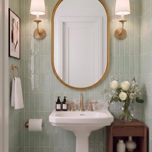 Puede incluir: Un baño con azulejos verticales de color verde claro, un lavabo de pedestal blanco con grifería de latón, un espejo ovalado con marco dorado, dos apliques de pared, un inodoro blanco y una mesa de madera con un jarrón de flores blancas.