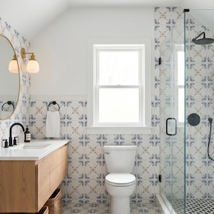 Könnte beinhalten: Ein modernes Badezimmer mit einem Holzwaschtisch, einer weißen Toilette und einer Glasdusche. Die Wände und der Boden weisen ein blau-weißes Blumenfliesenmuster auf. Ein runder Spiegel und goldene Leuchten ergänzen die Einrichtung.