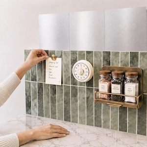 Peut inclure: Une installation murale de cuisine avec des carreaux verticaux verts, une minuterie analogique ronde crème et un support en métal laitonné contenant trois pots à épices en verre étiquetés Pink Salt, Black Pepper et Sea Salt, avec une note aimantée.