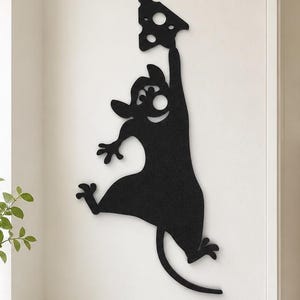 Peut inclure: Une décoration murale en métal noir représentant une souris stylisée qui tend un bras vers le haut pour tenir un morceau de fromage suisse triangulaire. La souris a de grandes oreilles, une longue queue et un œil circulaire découpé.