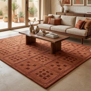 May include: A large rectangular area rug in a deep terracotta orange color featuring a repeating grid pattern of recessed squares. The rug is positioned on a light-colored floor in a living room setting, showcasing a textured, woven construction.
