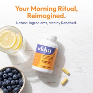 以下が含まれることがあります： 紫とオレンジ色のラベルが付いた「akka」サプリメントの白いボトル、レモンスライスが入ったグラス、ブルーベリーのボウル、2つの黄色のカプセル。テキストは「Your Morning Ritual, Reimagined.」と書かれています。
