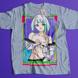 Puede incluir: Camiseta azul claro con una colorida ilustraci&oacute;n de estilo anime. El gr&aacute;fico presenta un personaje femenino con cabello azul y amarillo, sosteniendo un dispositivo. El dise&ntilde;o est&aacute; enmarcado con bordes verde ne&oacute;n y rosa, con texto de fondo.