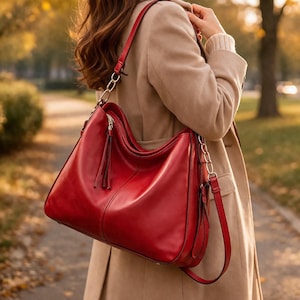 May include: A vibrant red leather shoulder bag with a gold chain strap and a matching adjustable shoulder strap. The bag features a zippered top closure and a decorative tassel. The bag is carried over the shoulder.