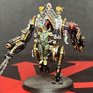 May include: A detailed miniature figure of a mechanical warrior, painted in black, gold, and silver. The figure has a detailed cockpit with a pilot inside. The figure is mounted on a black circular base. The figure has two arms, one with a gun and the other with a claw.